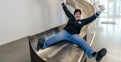 Person with arms raised, smiling while sliding down a large indoor metal slide at White Castle headquarters in Columbus, Ohio.