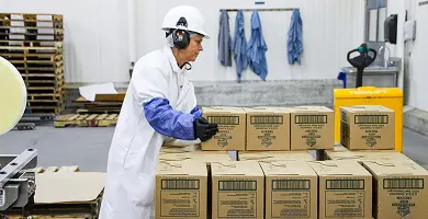 Factory worker in protective gear stacking White Castle food boxes on a pallet in a production facility.