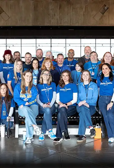 Large group of White Castle team members in blue shirts pose together for a group photo at an indoor event.