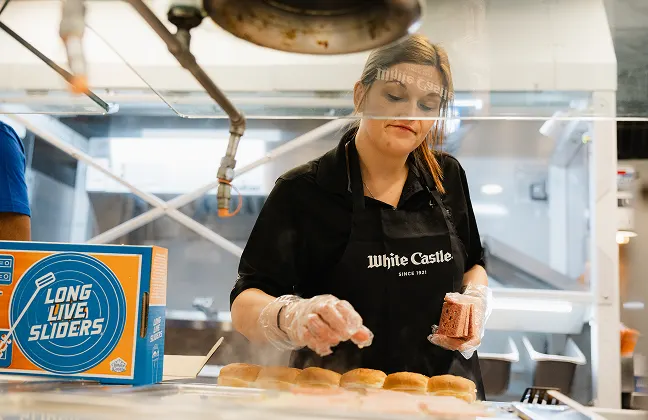 White Castle employee assembles sliders behind a protective counter in the restaurant kitchen.