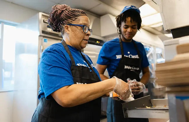 Two White Castle employees smile while preparing sliders together in the kitchen.