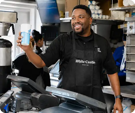 White Castle employee smiles while holding a drink cup behind the restaurant counter.