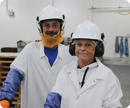 Two food production workers in protective gear smile inside a White Castle manufacturing facility.